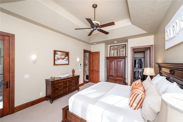 carpeted bedroom featuring a walk in closet, a tray ceiling, a closet, and ceiling fan