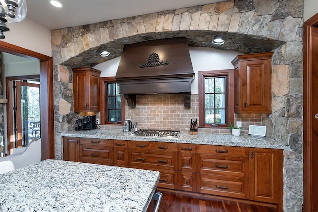 kitchen featuring decorative backsplash, premium range hood, light stone counters, stainless steel gas cooktop, and dark hardwood / wood-style floors