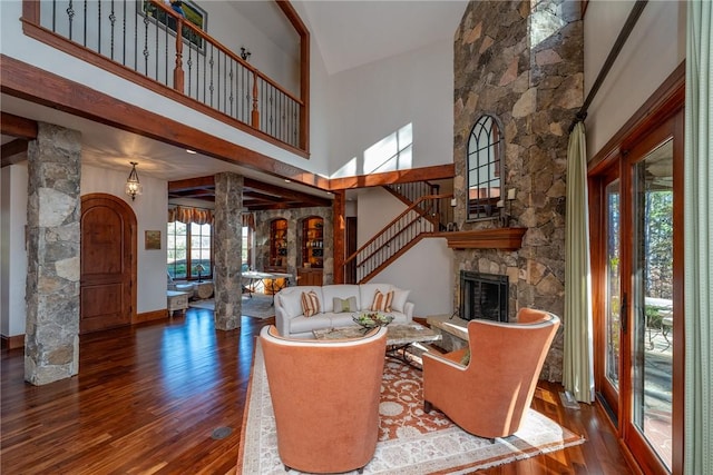 living room with ornate columns, a stone fireplace, a towering ceiling, and dark wood-type flooring