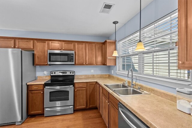 kitchen with hanging light fixtures, sink, stainless steel appliances, and light hardwood / wood-style floors