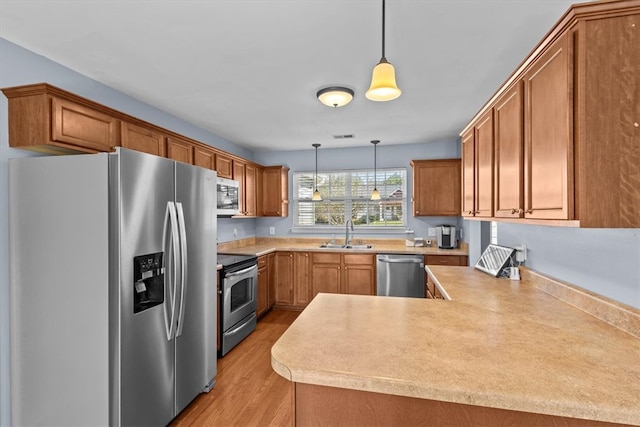 kitchen featuring kitchen peninsula, appliances with stainless steel finishes, sink, pendant lighting, and light hardwood / wood-style flooring