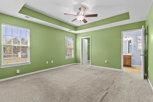 unfurnished bedroom with light colored carpet, ensuite bath, and a tray ceiling