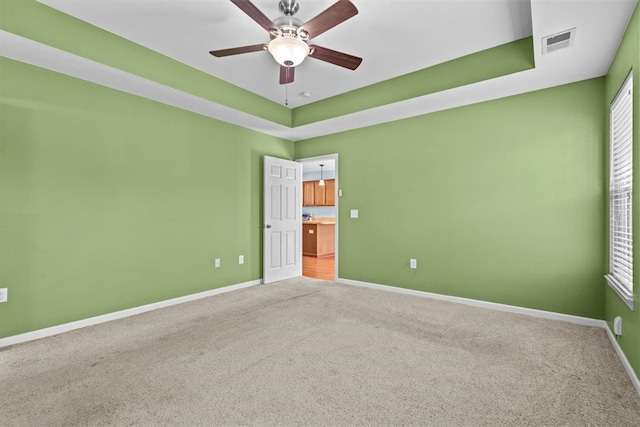 carpeted empty room featuring a raised ceiling and ceiling fan