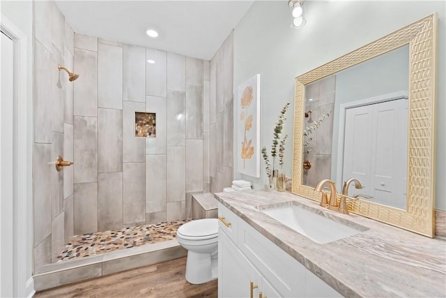 bathroom featuring a tile shower, hardwood / wood-style floors, vanity, and toilet