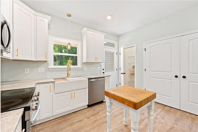 kitchen with sink, hanging light fixtures, stainless steel appliances, light hardwood / wood-style flooring, and white cabinets