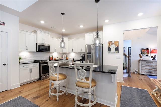 kitchen with appliances with stainless steel finishes, light wood-type flooring, pendant lighting, white cabinetry, and a kitchen island