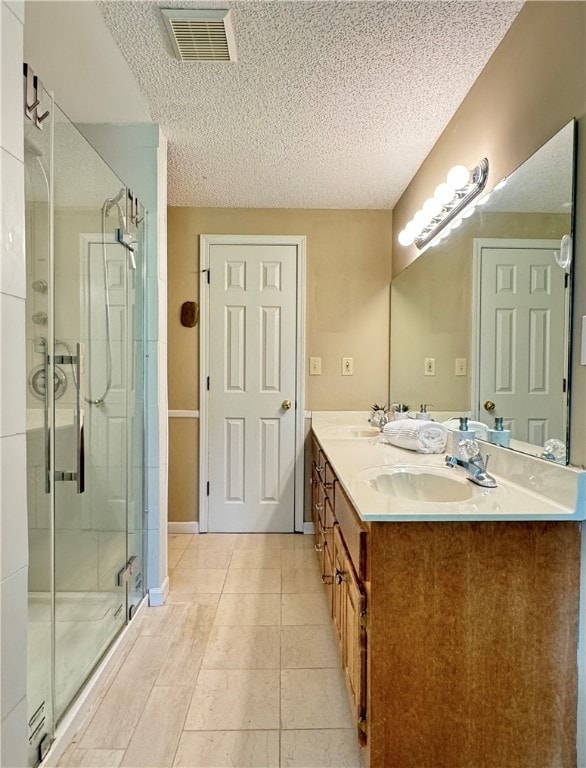 bathroom with a shower with door, vanity, a textured ceiling, and tile patterned flooring