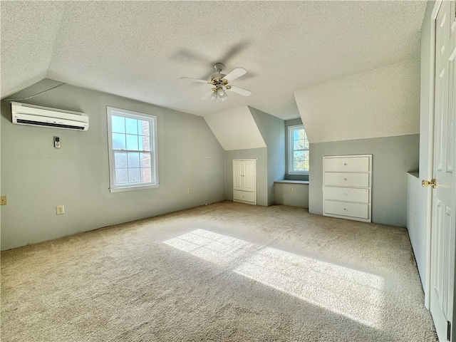 additional living space featuring vaulted ceiling, light colored carpet, a textured ceiling, and a wall mounted AC