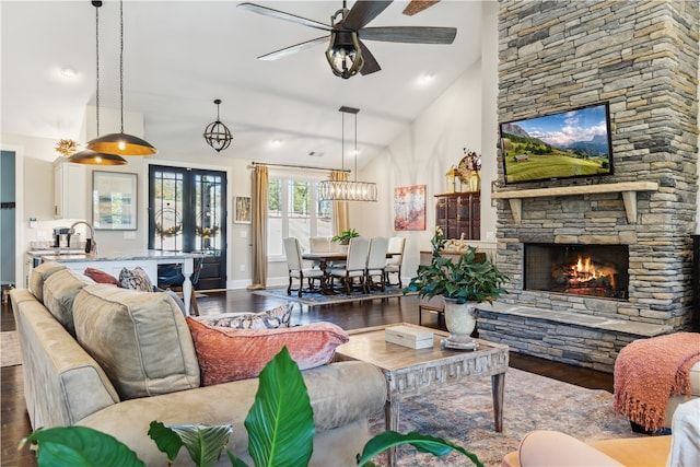 living room featuring hardwood / wood-style flooring, ceiling fan, a stone fireplace, and vaulted ceiling