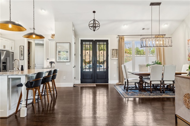 kitchen with light stone countertops, white cabinets, stainless steel fridge with ice dispenser, dark hardwood / wood-style floors, and hanging light fixtures