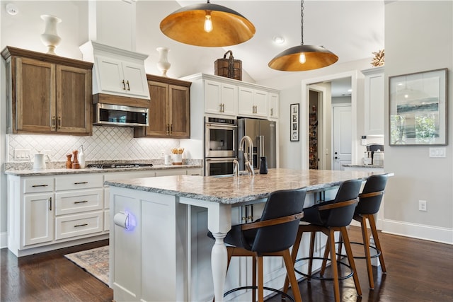 kitchen with light stone countertops, white cabinetry, hanging light fixtures, a center island with sink, and appliances with stainless steel finishes