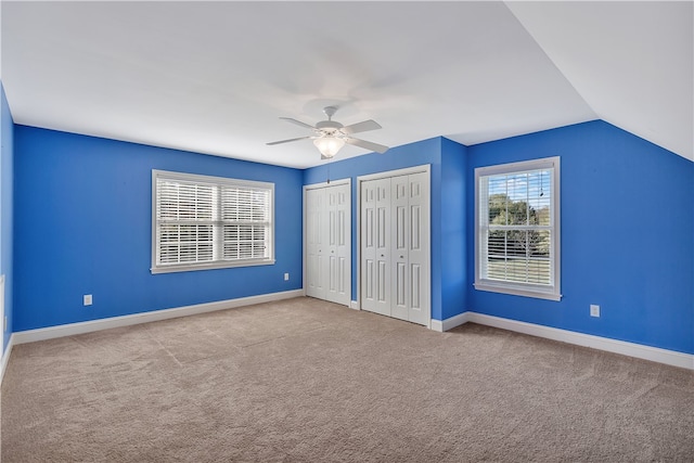 unfurnished bedroom with ceiling fan, light colored carpet, lofted ceiling, and two closets