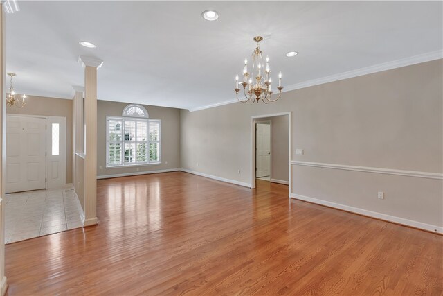 unfurnished living room featuring ornate columns, crown molding, light hardwood / wood-style floors, and an inviting chandelier