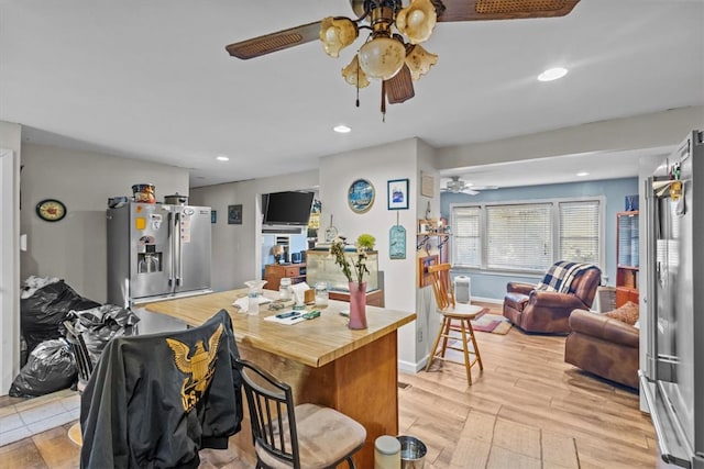 kitchen featuring ceiling fan, stainless steel refrigerator with ice dispenser, butcher block countertops, light hardwood / wood-style floors, and a breakfast bar area