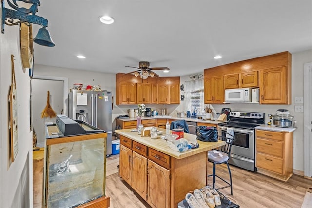 kitchen featuring ceiling fan, light hardwood / wood-style floors, appliances with stainless steel finishes, a kitchen island, and a breakfast bar area