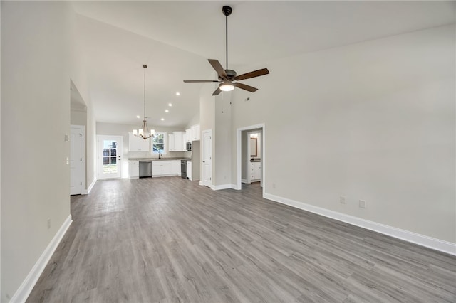 unfurnished living room with hardwood / wood-style flooring, ceiling fan with notable chandelier, sink, and high vaulted ceiling