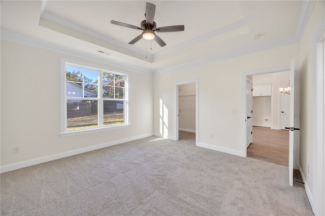 unfurnished bedroom featuring a tray ceiling, a spacious closet, ceiling fan, and crown molding