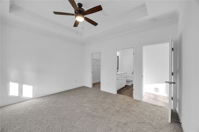 unfurnished bedroom with ensuite bathroom, a walk in closet, crown molding, ceiling fan, and a tray ceiling