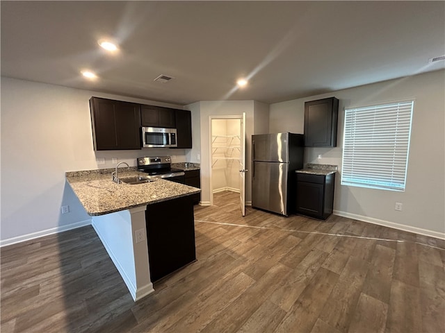 kitchen with light stone countertops, sink, kitchen peninsula, hardwood / wood-style floors, and appliances with stainless steel finishes