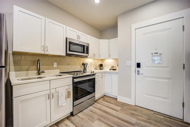 kitchen with white cabinetry, sink, backsplash, light hardwood / wood-style floors, and appliances with stainless steel finishes