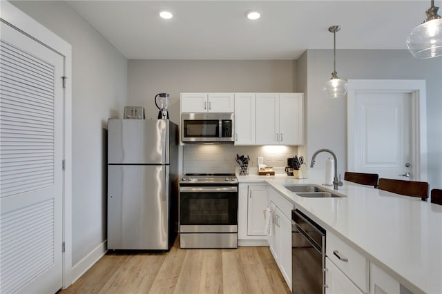 kitchen with appliances with stainless steel finishes, sink, pendant lighting, white cabinets, and light hardwood / wood-style floors