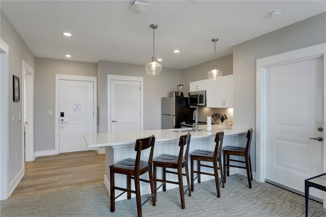 kitchen with pendant lighting, kitchen peninsula, light hardwood / wood-style flooring, appliances with stainless steel finishes, and white cabinetry