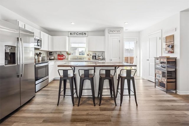 kitchen with wood finished floors, white cabinetry, a kitchen breakfast bar, light countertops, and appliances with stainless steel finishes