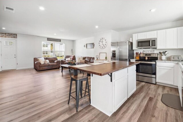 kitchen featuring a breakfast bar area, appliances with stainless steel finishes, light hardwood / wood-style floors, white cabinets, and wood counters