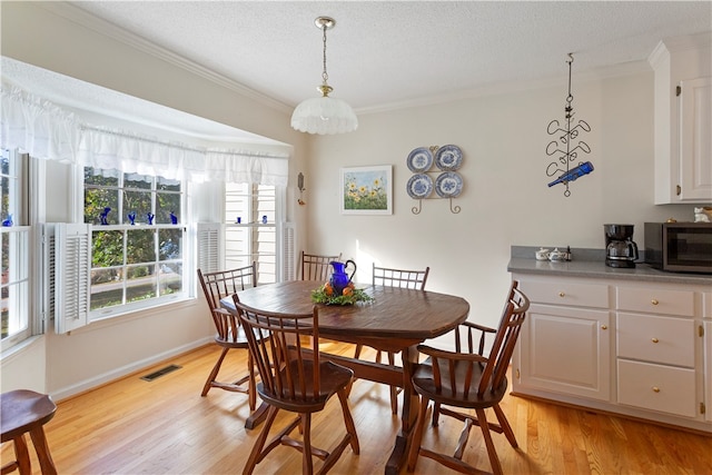 dining room with a textured ceiling, light hardwood / wood-style flooring, and ornamental molding