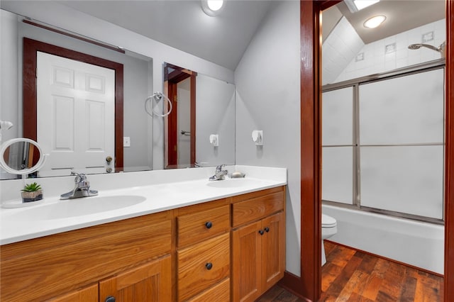 full bathroom with bath / shower combo with glass door, vanity, hardwood / wood-style flooring, toilet, and lofted ceiling