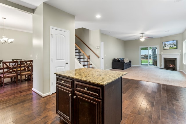 kitchen with ceiling fan with notable chandelier, dark hardwood / wood-style floors, light stone countertops, decorative light fixtures, and a kitchen island