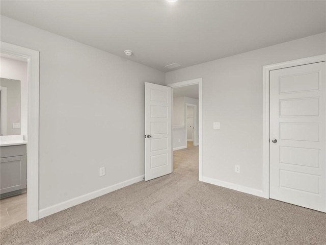 unfurnished bedroom with light colored carpet and connected bathroom