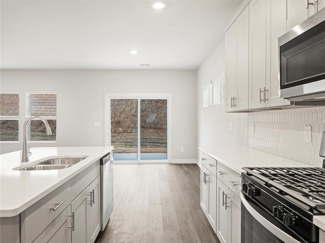 kitchen featuring sink, light hardwood / wood-style flooring, appliances with stainless steel finishes, white cabinetry, and backsplash