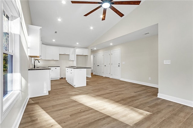 kitchen with light wood-type flooring, a kitchen island, ceiling fan, high vaulted ceiling, and white cabinetry