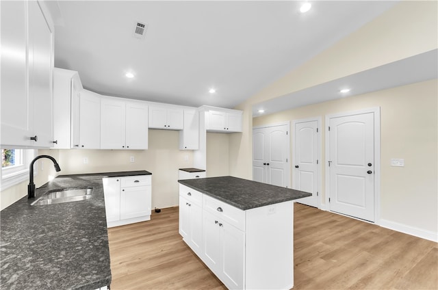 kitchen with sink, a center island, lofted ceiling, white cabinets, and light wood-type flooring