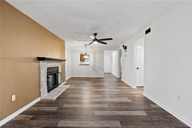 unfurnished living room with a stone fireplace, ceiling fan, and dark hardwood / wood-style flooring