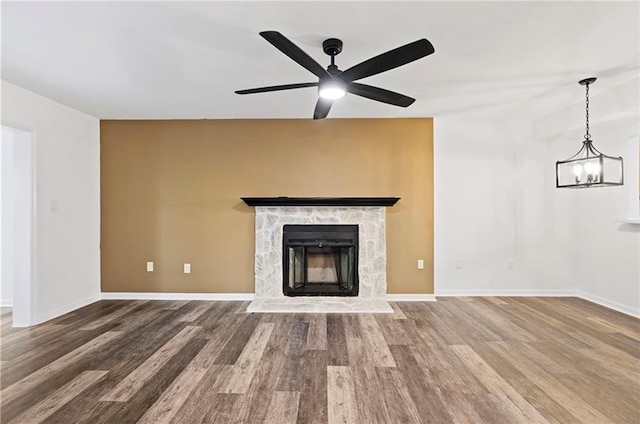 unfurnished living room with hardwood / wood-style floors, ceiling fan with notable chandelier, and a stone fireplace