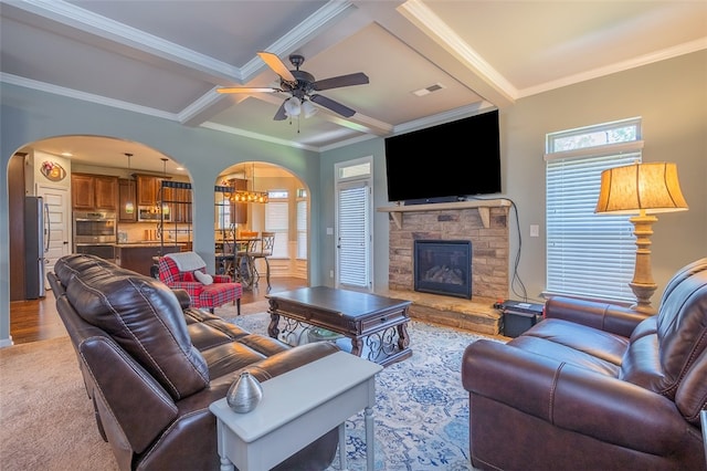 living room with ornamental molding, ceiling fan with notable chandelier, light hardwood / wood-style flooring, beamed ceiling, and a fireplace