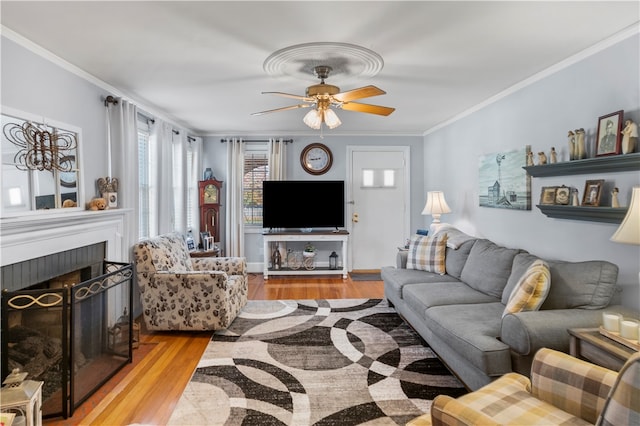 living room featuring ceiling fan, light hardwood / wood-style flooring, ornamental molding, and a brick fireplace