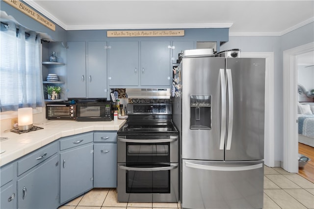 kitchen featuring ventilation hood, stainless steel appliances, blue cabinets, crown molding, and tile countertops