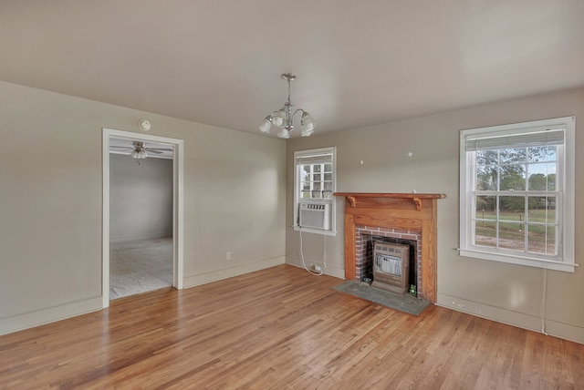 unfurnished living room featuring ceiling fan with notable chandelier, cooling unit, light wood-type flooring, and a brick fireplace