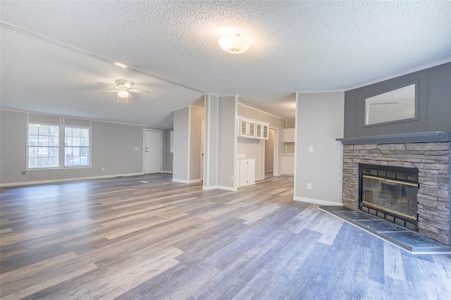 unfurnished living room with wood-type flooring, a textured ceiling, a stone fireplace, and ceiling fan