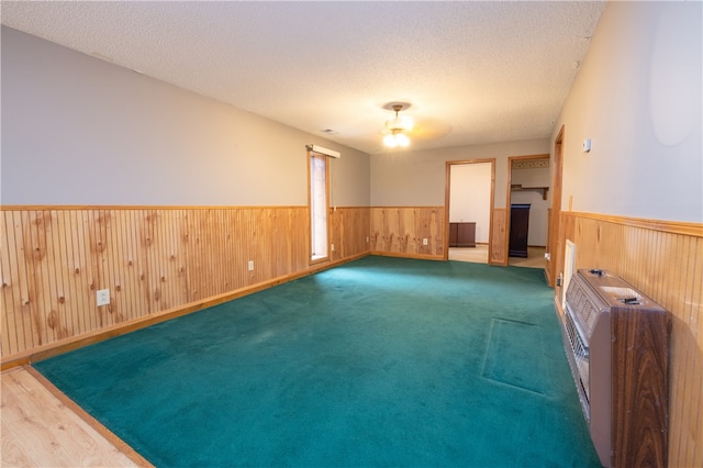 spare room with hardwood / wood-style flooring, wood walls, a textured ceiling, and heating unit