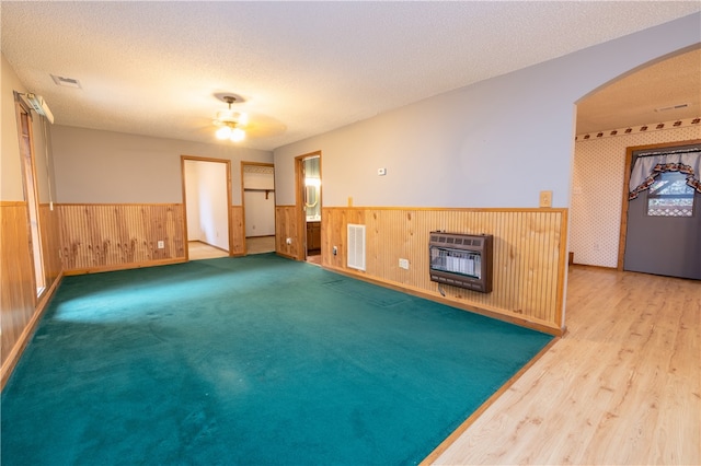 empty room featuring hardwood / wood-style floors, wood walls, ceiling fan, a textured ceiling, and heating unit