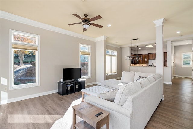 living room featuring hardwood / wood-style flooring, ceiling fan, crown molding, and decorative columns