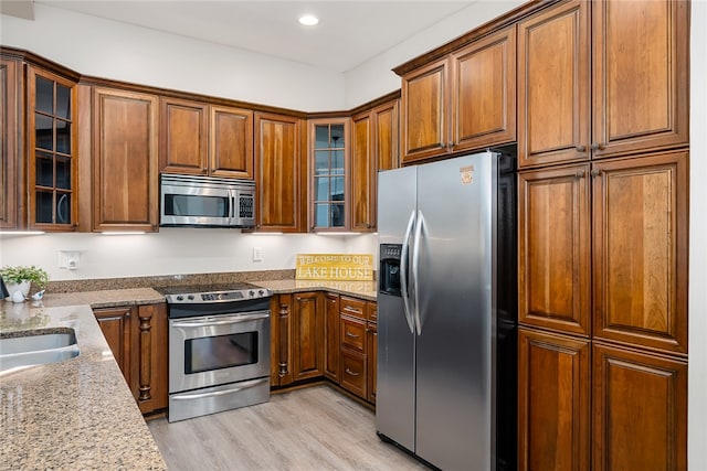 kitchen featuring light stone countertops, sink, stainless steel appliances, and light wood-type flooring