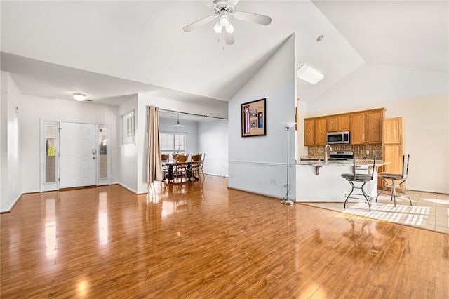 living room with ceiling fan, high vaulted ceiling, and light wood-type flooring