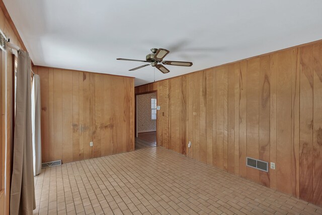 empty room featuring ceiling fan and wood walls