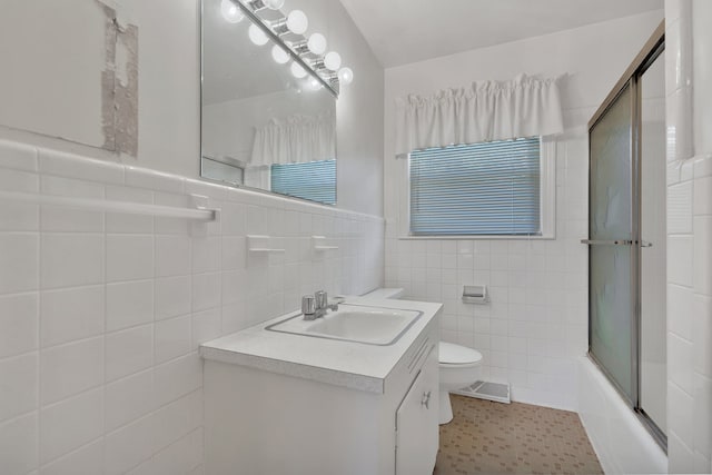 full bathroom featuring shower / bath combination with glass door, vanity, toilet, and tile walls