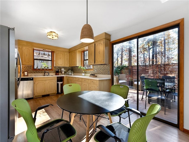 kitchen with tasteful backsplash, stainless steel appliances, sink, light hardwood / wood-style flooring, and hanging light fixtures